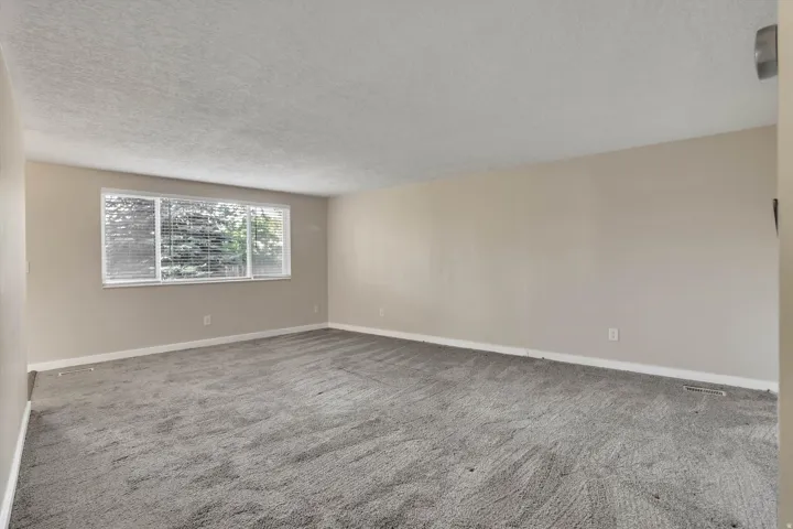 Spacious room featuring neutral painted walls, light gray carpeting, and a large window with horizontal blinds