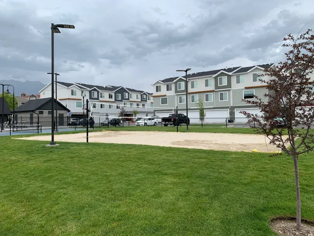 Expansive green space featuring a sand volleyball court, tennis court, and a detached structure