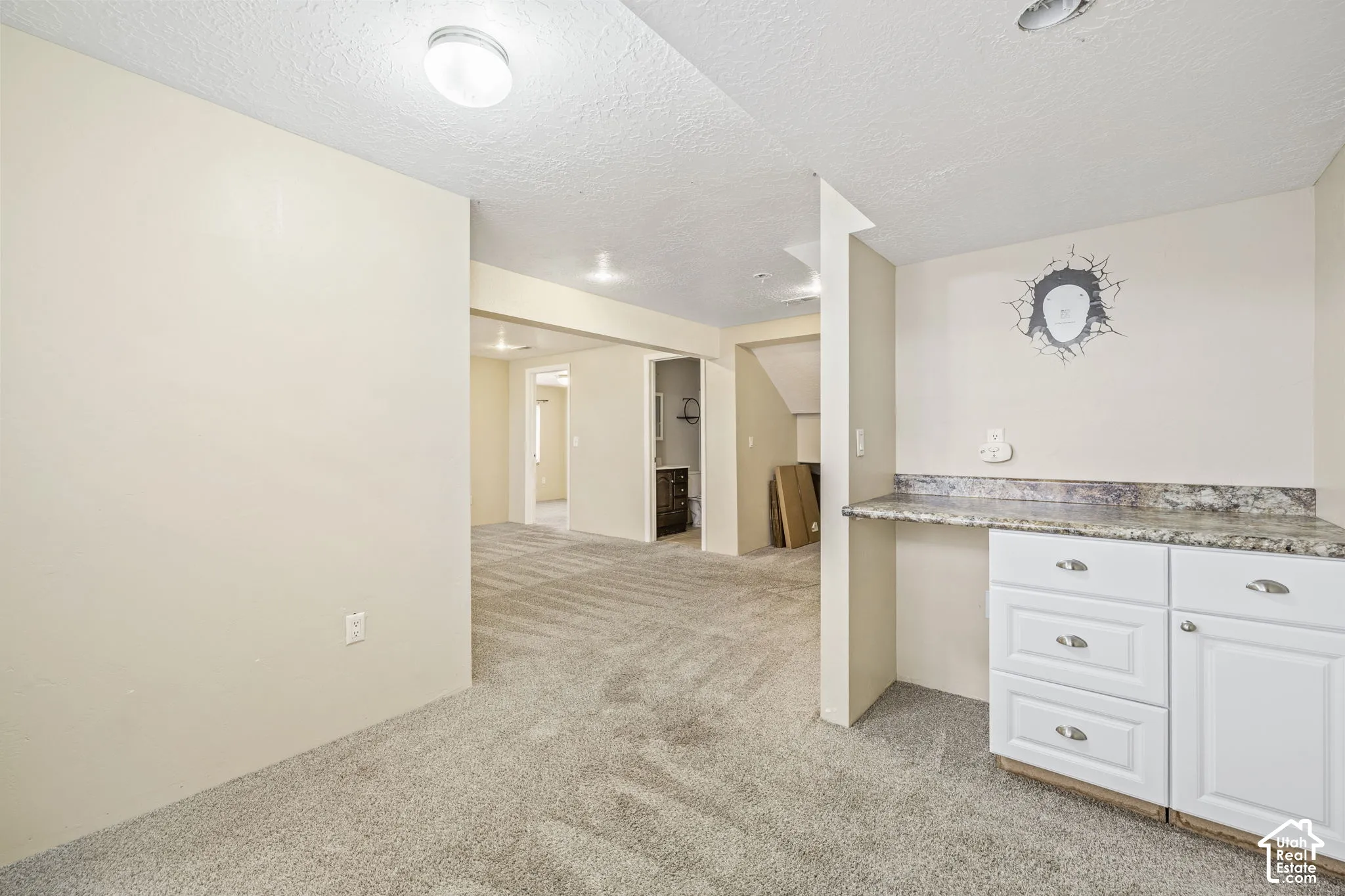 Recessed lighting and flush-mount fixtures illuminate the space, featuring white cabinetry, a stone-finish countertop, and wall-to-wall carpeting