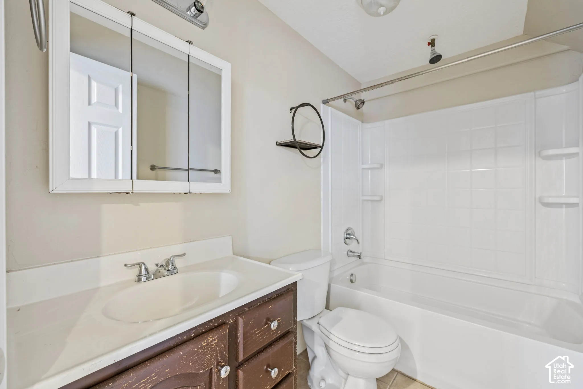 Vanity with integrated sink, tri-fold medicine cabinet, and a shower/tub combination with white surround