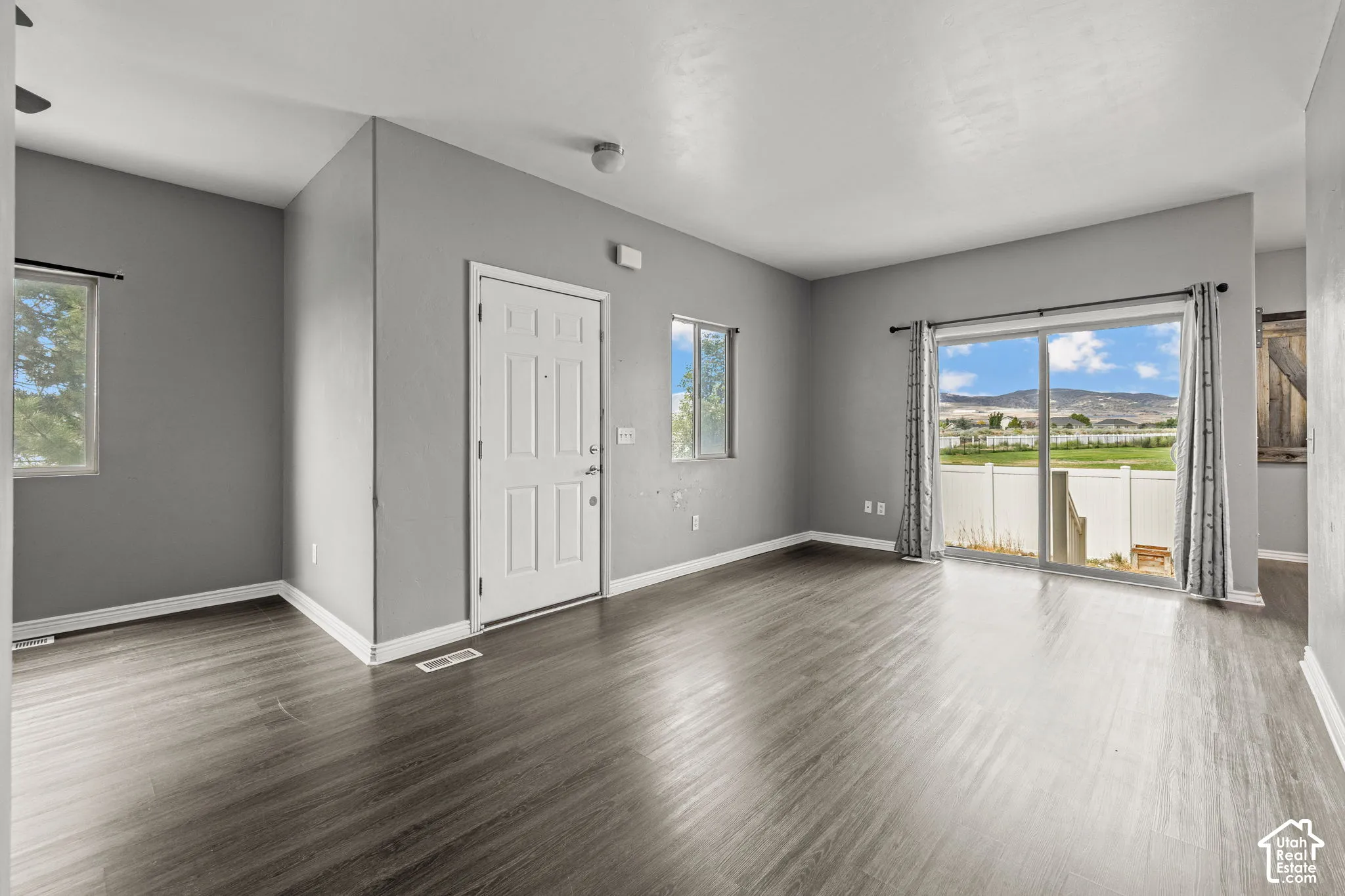Expansive living area featuring wood-finish flooring, a white paneled entry door, a large sliding glass door, and multiple windows providing ambient light