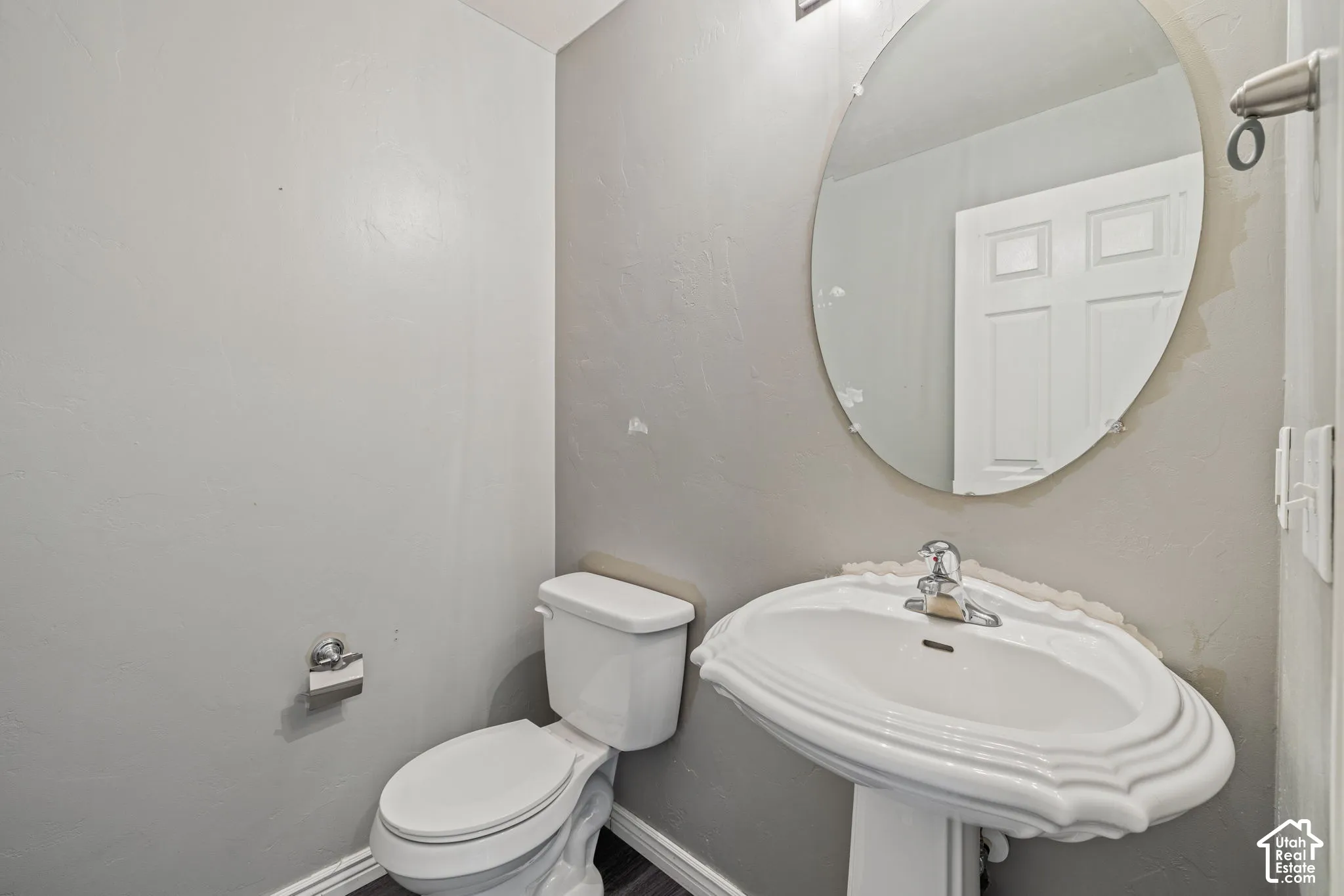 Pedestal sink with chrome faucet, oval frameless mirror, and dark wood-finish flooring