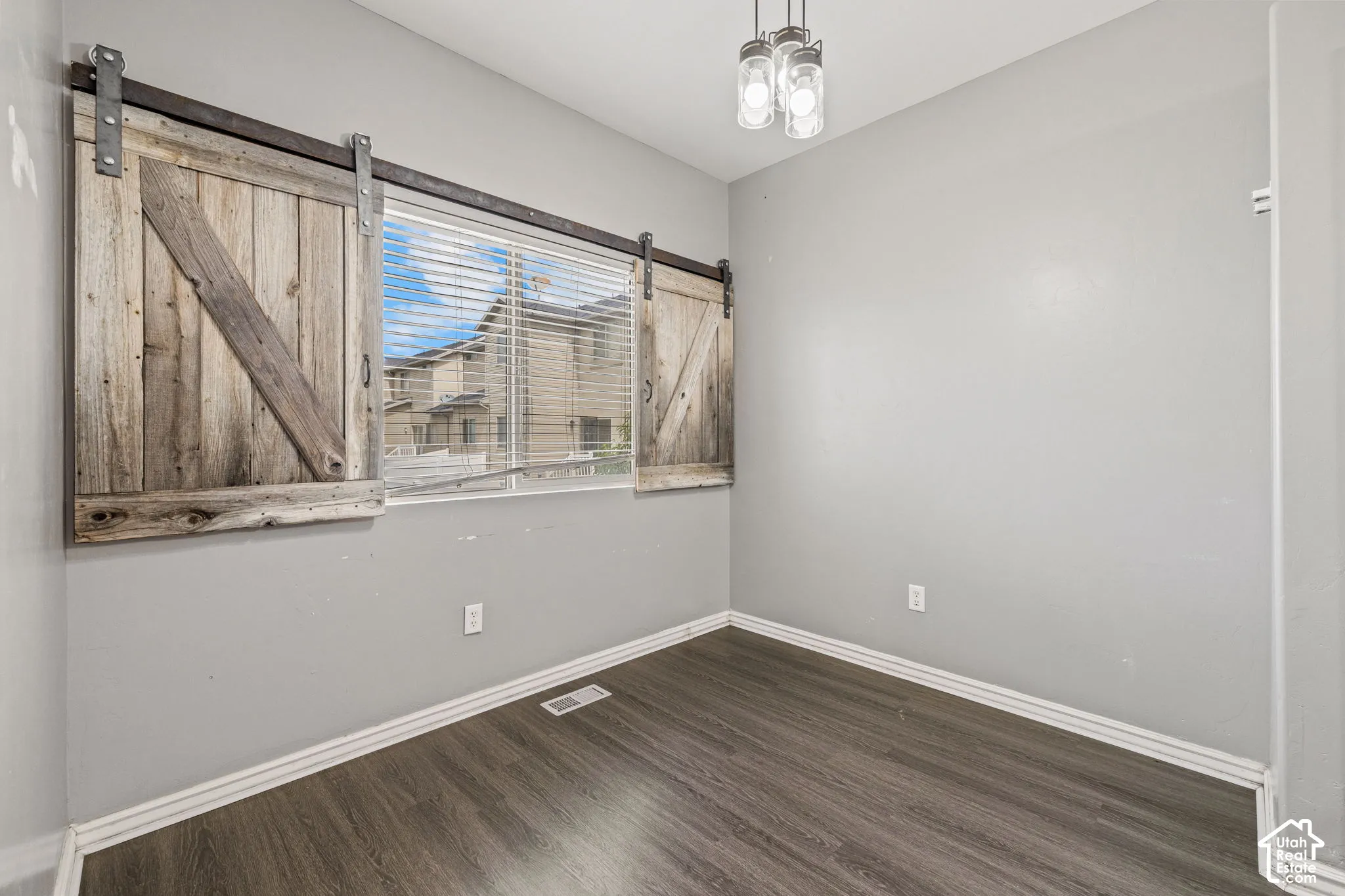 Wood-finish flooring with light gray walls, complemented by a window featuring barn door-style shutters