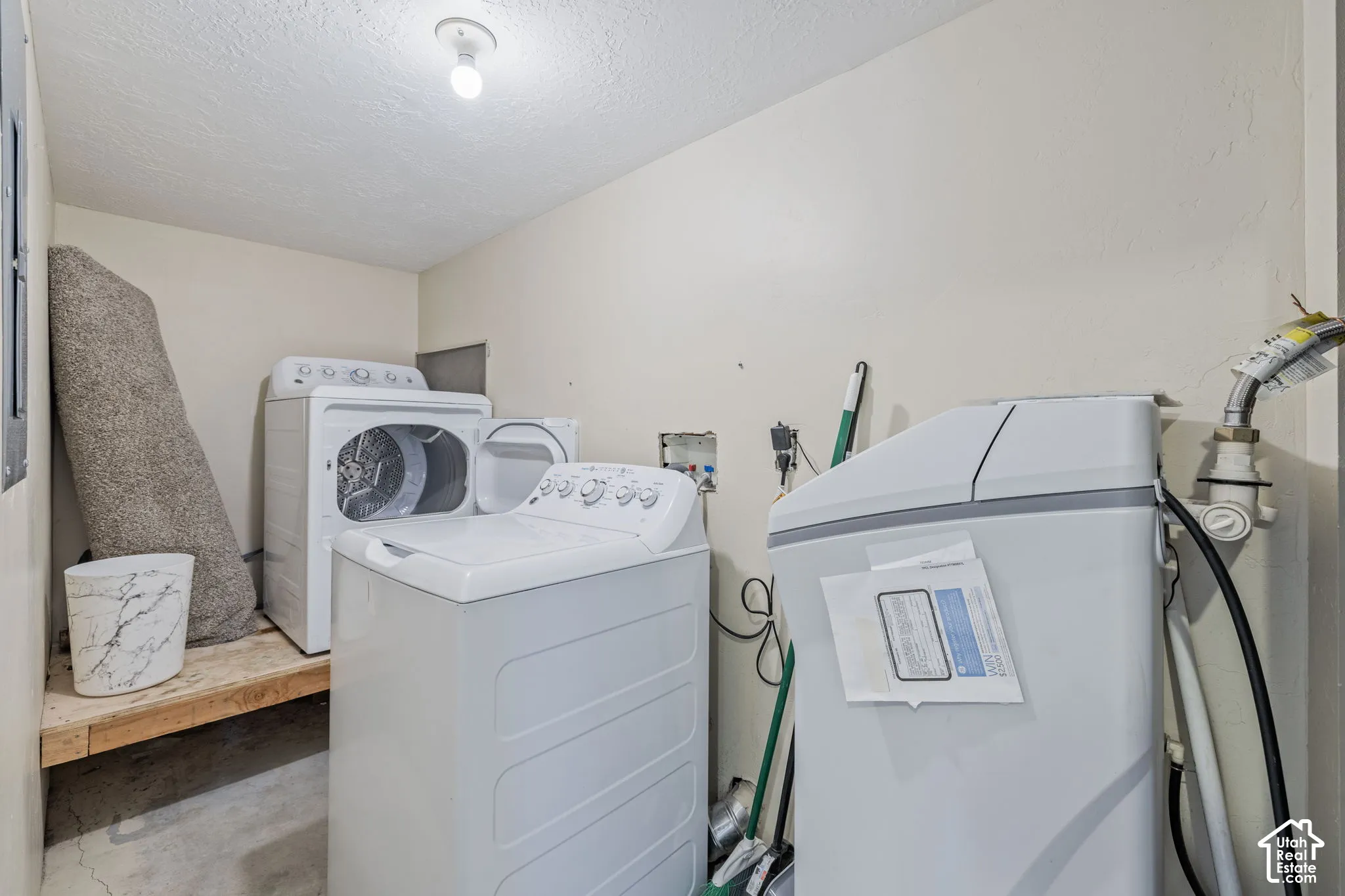 Laundry area with concrete flooring, built-in wooden shelf, and surface-mounted ceiling light