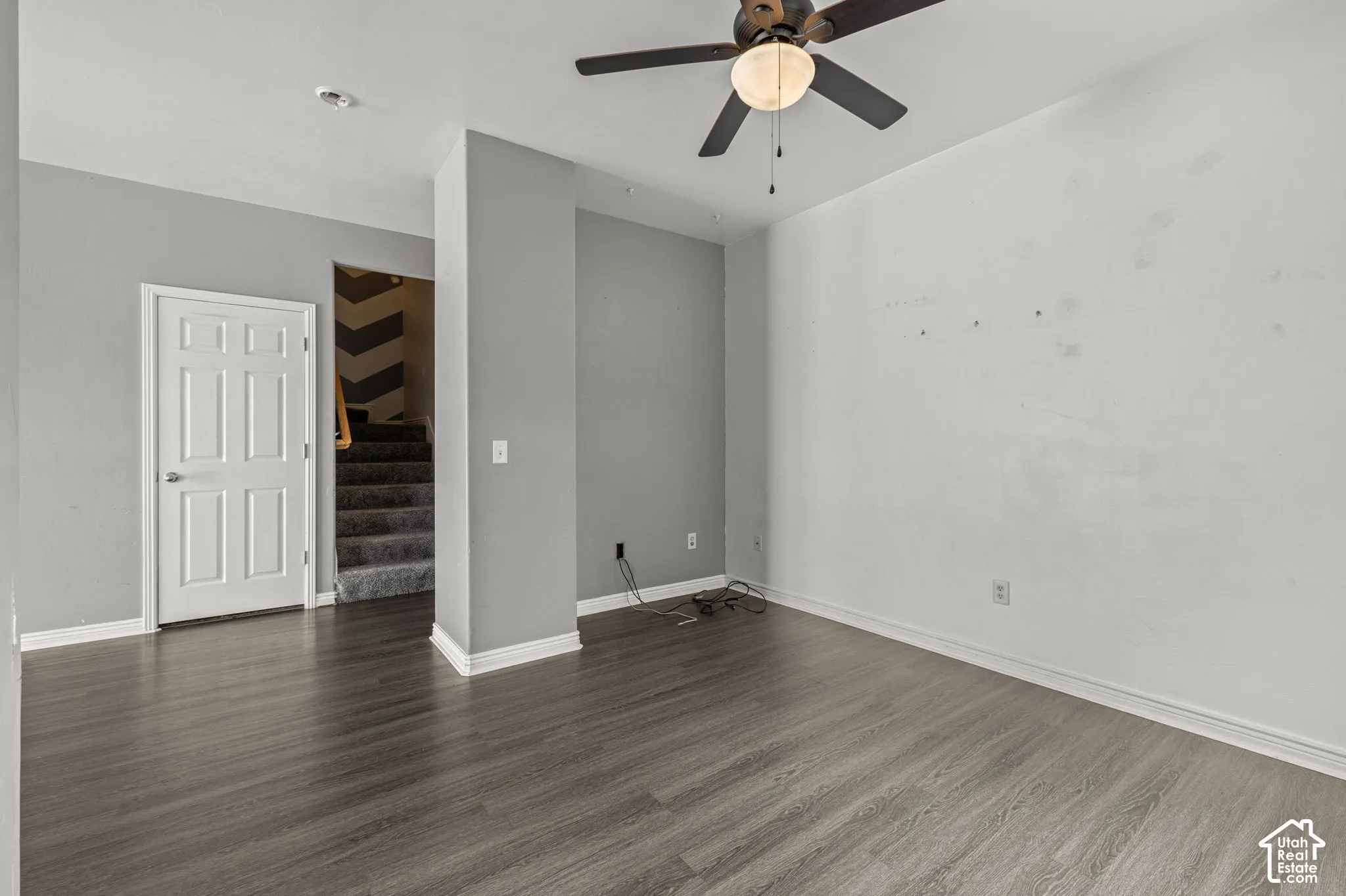Wood-finish flooring throughout, ceiling fan with integrated lighting, white trim and baseboards, paneled interior door, and carpeted stairs