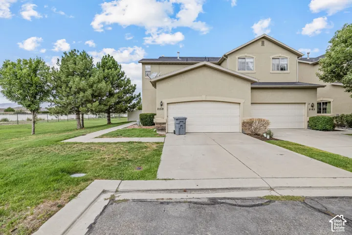 Stucco exterior with multiple windows, attached garage, concrete driveway, and mature landscaping