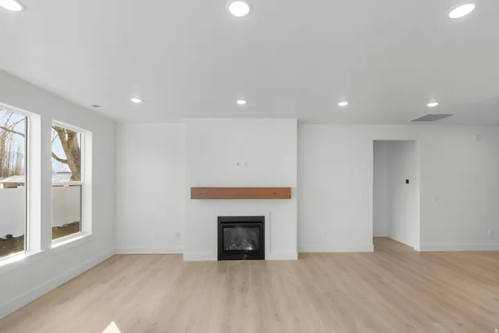Spacious room with light wood-finish flooring, multiple windows, recessed ceiling lighting, and a modern fireplace with a wood mantel