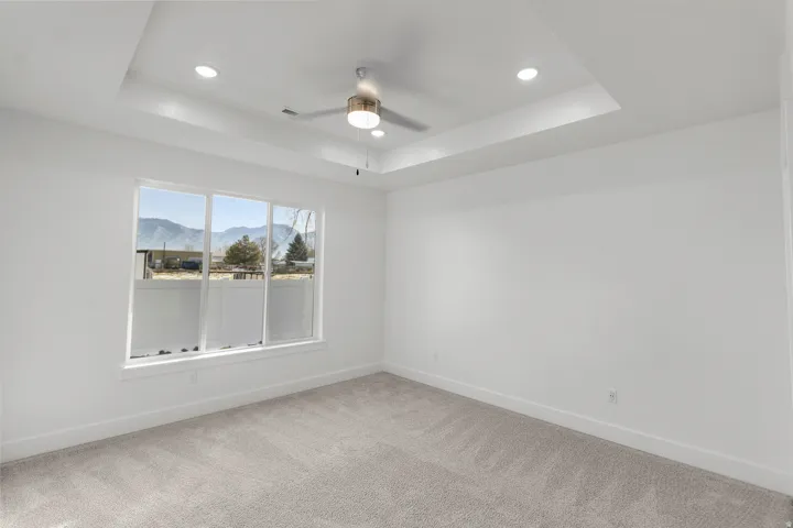 Tray ceiling with recessed lighting, ceiling fan, large picture window, and neutral carpet