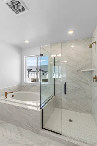 Floor-to-ceiling marble-look tile, built-in soaking tub, walk-in shower with clear glass enclosure, brass-finish fixtures, and recessed lighting
