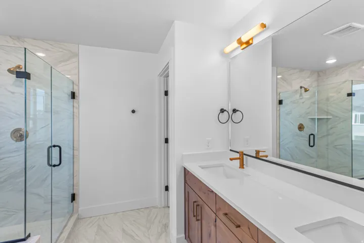 Dual glass-enclosed shower stalls with brass fixtures, a double vanity with an integrated sink, white countertops, and wood-finish cabinetry