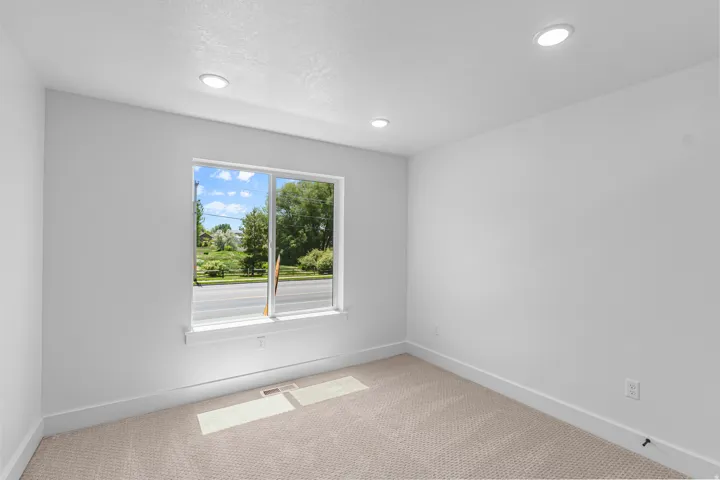 Recessed lighting, neutral wall paint, light-toned carpeting, and a window with white trim