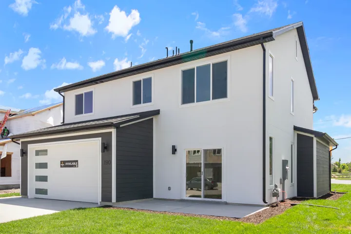 Two-story residence featuring a white stucco exterior, dark siding accents, and a modern garage door with frosted glass panels