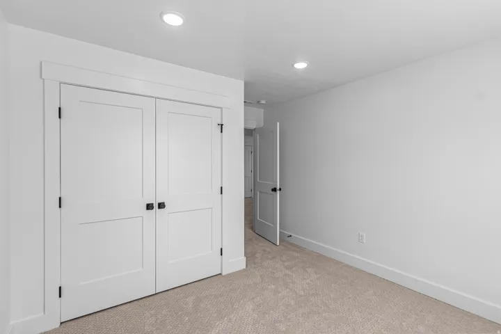 Recessed lighting, light-toned carpeting, white walls, white paneled doors, and contrasting dark hardware