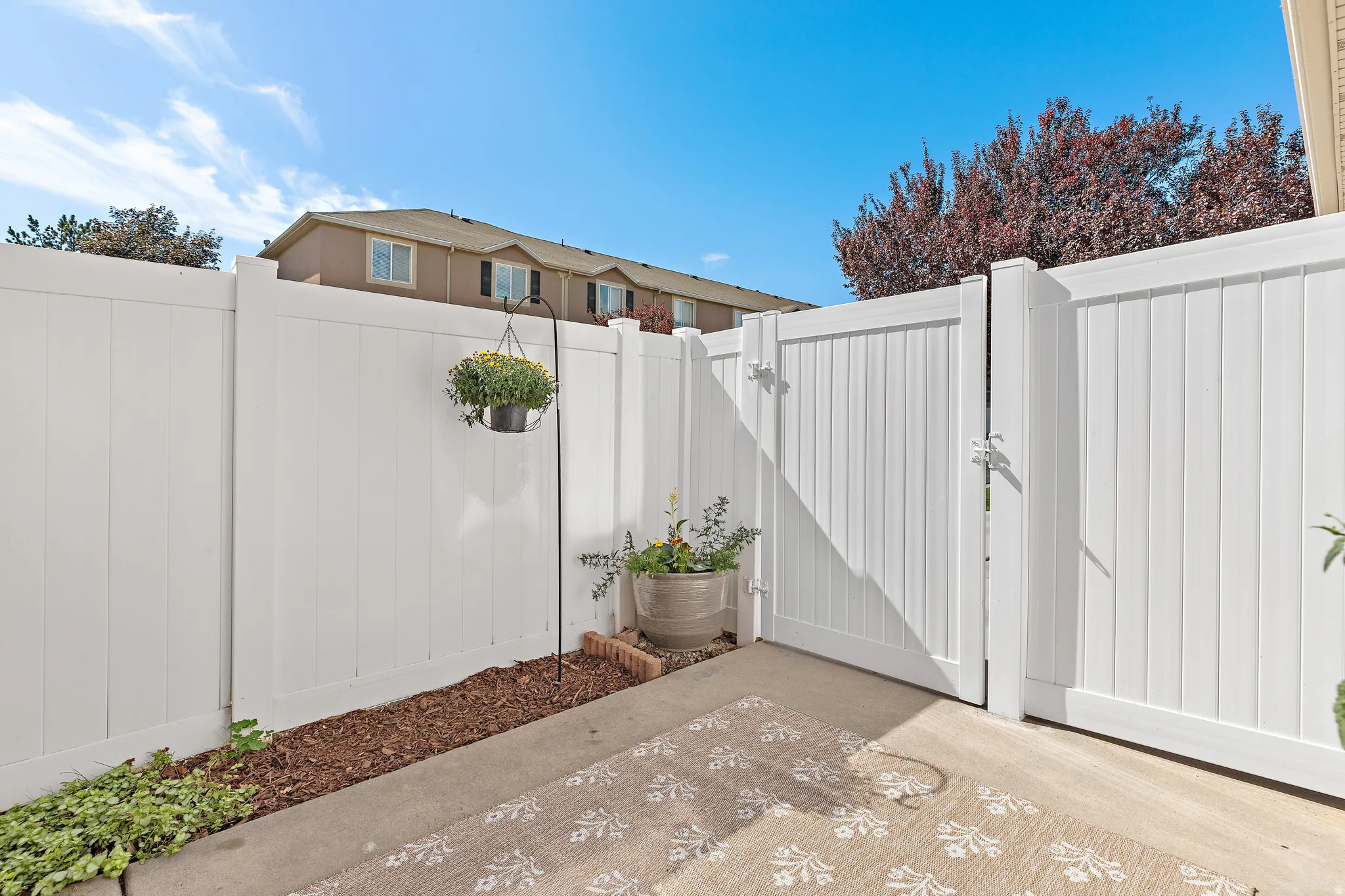 Spacious private patio featuring a white fence, flower bed and gate to driveway