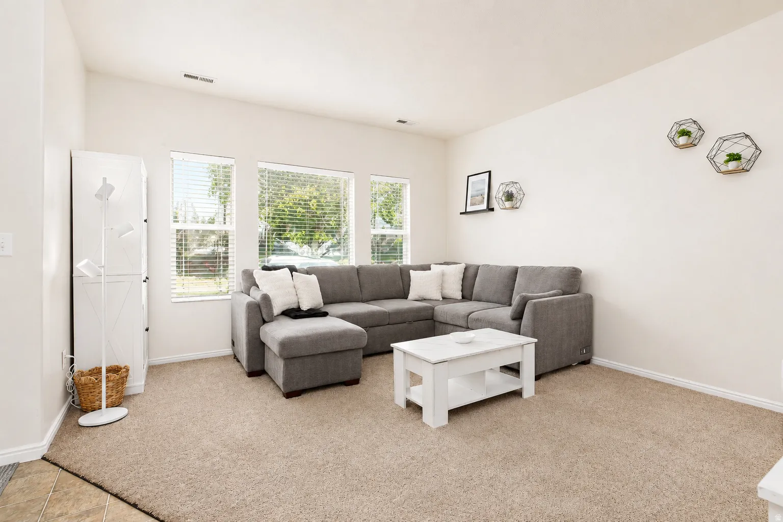 Bright spacious living area featuring carpeted flooring and multiple windows offering natural light with blinds