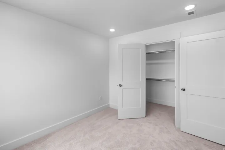 Neutral-toned carpet flooring, recessed ceiling lights, and a closet featuring a white flat-panel door with metal hardware and built-in shelving