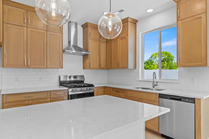 Kitchen featuring natural wood cabinetry, white subway tile backsplash, stainless steel appliances, and a central island with a white countertop