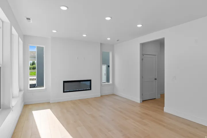 Recessed lighting, wood-finish flooring, linear electric fireplace, multiple tall windows, and white walls