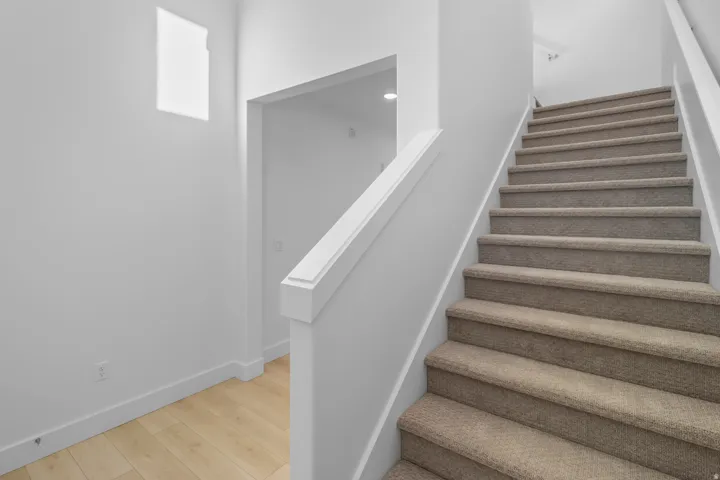 Carpeted staircase with a white handrail, light wood-finish flooring, and crisp white walls