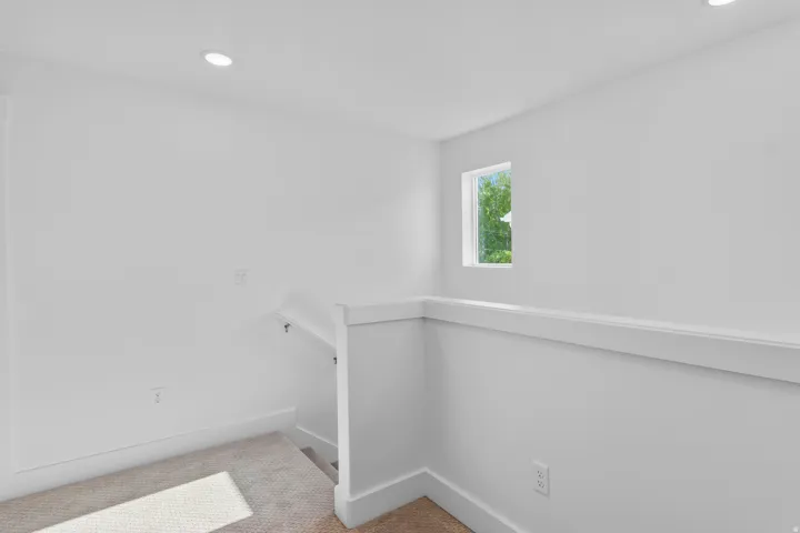 Recessed ceiling lighting, white painted walls, natural light from a window, and carpeted flooring
