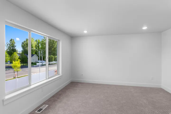 Spacious room featuring a large multi-pane window, recessed ceiling lighting, light gray carpet, and white walls