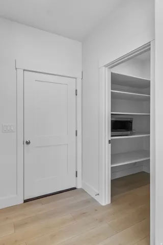 White interior doors with panel details, light wood-finish flooring, and a built-in pantry with shelving