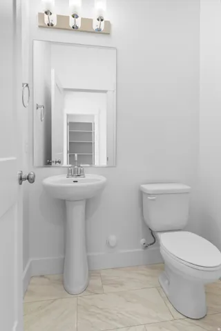 Pedestal sink, wall-mounted rectangular mirror, three-light vanity fixture, white toilet, and tiled flooring