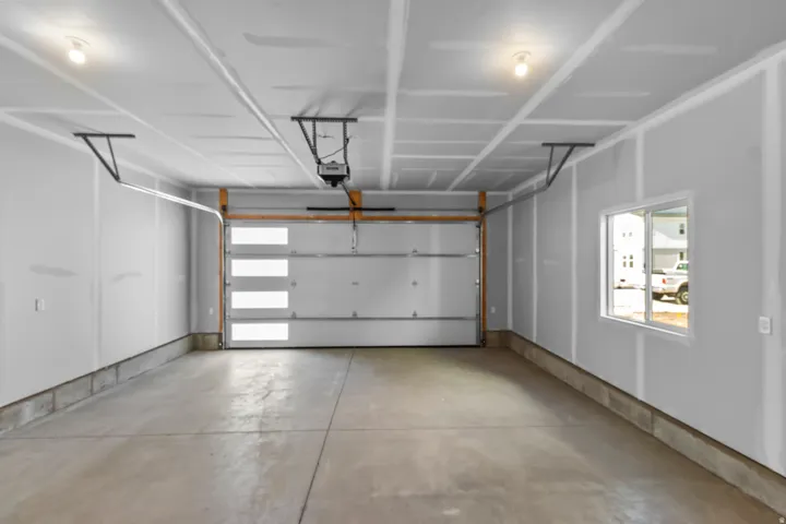 Concrete flooring, overhead lighting, modern garage door with frosted panels, and a fixed pane window