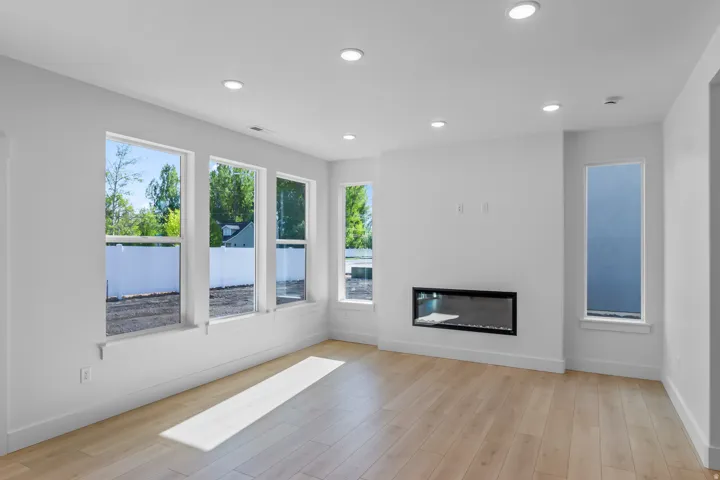 Recessed lighting illuminates an open living area featuring wood-finish flooring, a linear electric fireplace, and multiple windows