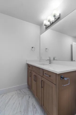 Wood-finish vanity with a white countertop and integrated sink, complemented by a large wall mirror and multi-bulb vanity lighting
