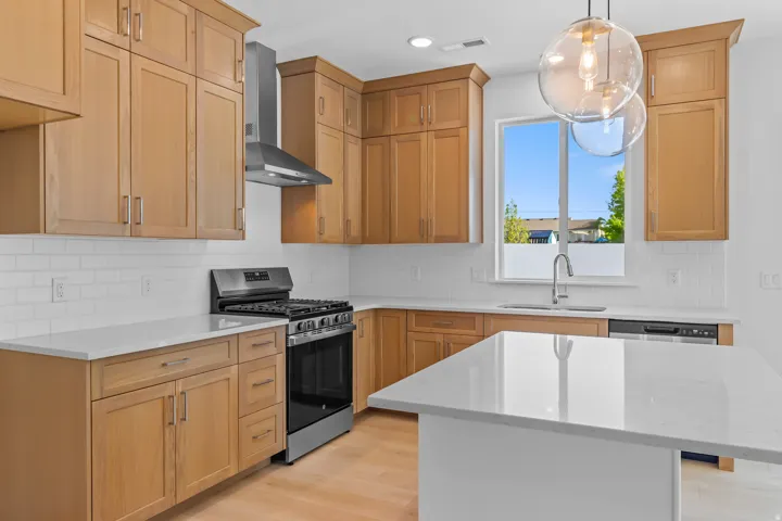 Kitchen featuring light wood cabinetry, stainless steel appliances, white subway tile backsplash, and a central island with a solid surface countertop