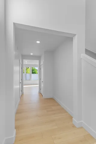Hallway featuring light wood-finish flooring, recessed lighting, white walls, and bright natural light at the far end