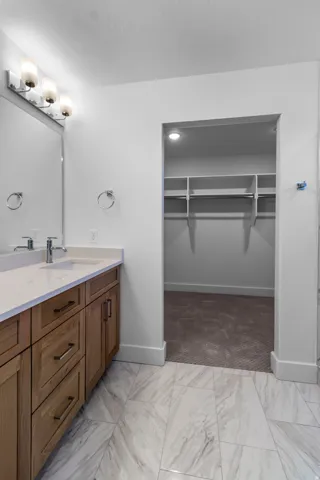 Light wood-finish vanity with a light countertop, a single basin sink, and a wall-mounted light fixture