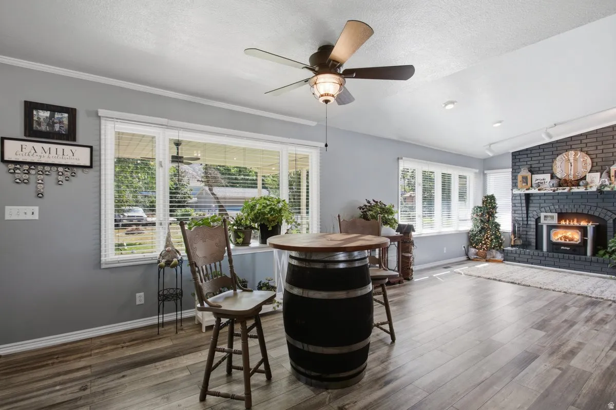 Wood-finish laminate flooring, multiple windows with blinds, recessed lighting, and a dark brick fireplace with a wood-burning insert