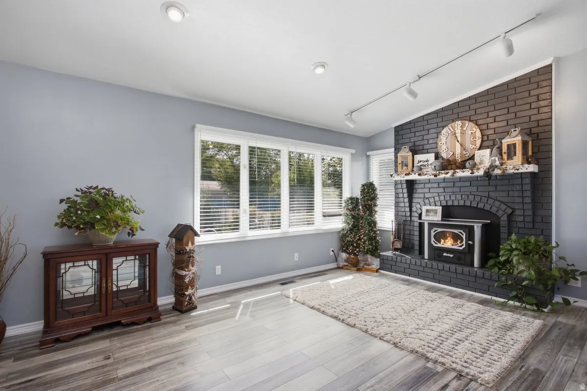 Painted brick fireplace with mantel, recessed lighting, track lighting, wood-finish flooring, and large windows