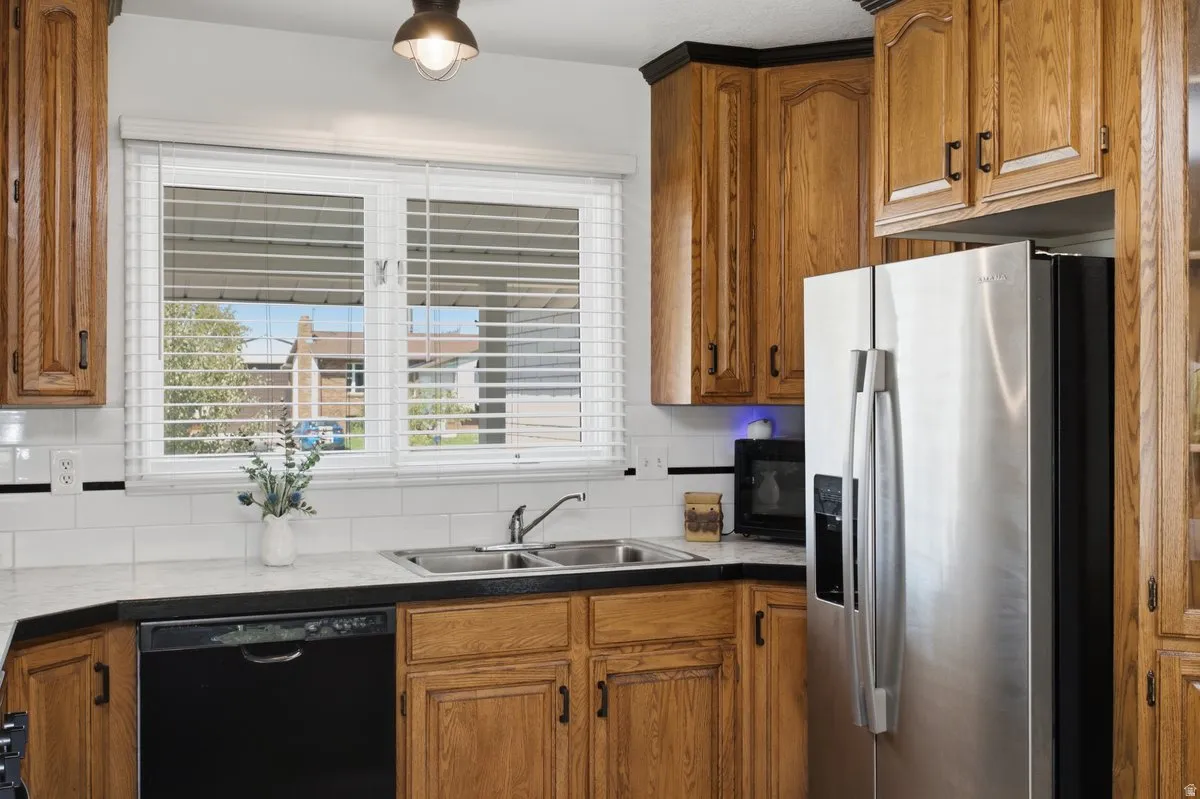 Kitchen featuring wood cabinetry, a double basin sink, white subway tile backsplash, and stainless steel refrigerator