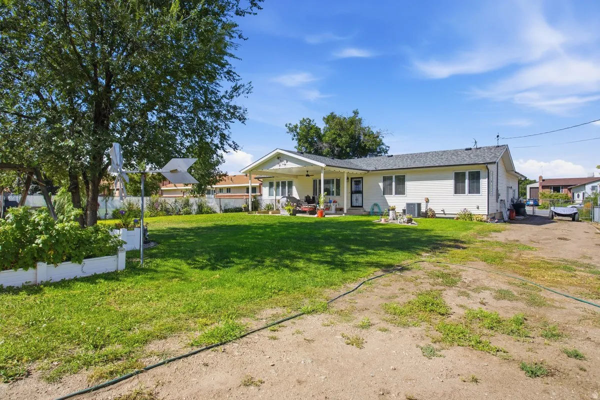 Expansive back yard with green lawn, white exterior siding, covered patio with outdoor ceiling fan, and mature trees