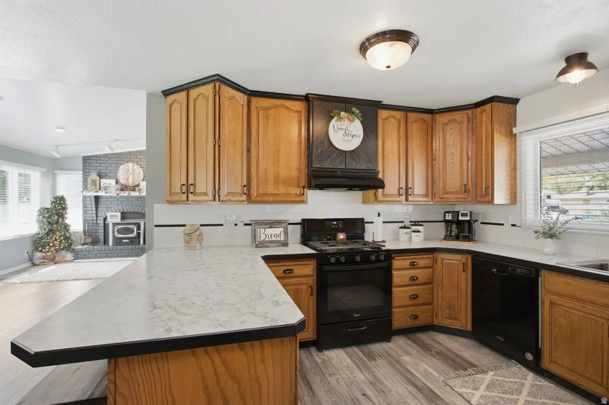 Wood-finish flooring, L-shaped white countertop, light wood cabinetry, black appliances, and white subway tile backsplash