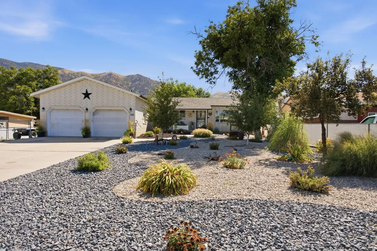 Expansive gravel landscaping with varied plantings, a two-car garage with white doors, and a concrete driveway