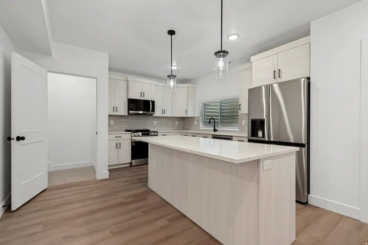 Contemporary kitchen featuring wood-finish flooring, a central island with a light-toned countertop, stainless steel appliances, and pendant lighting