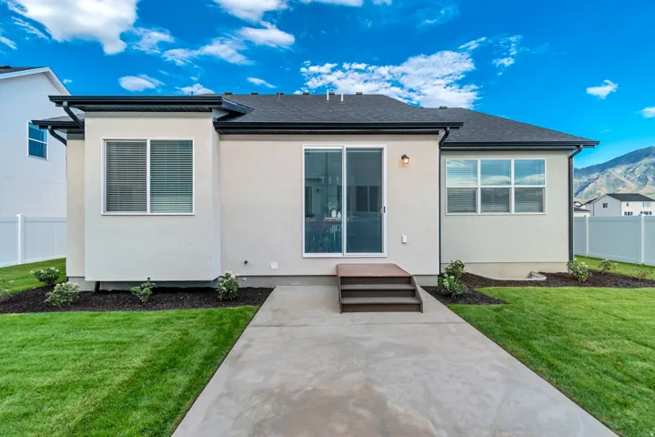 Expansive backyard featuring a concrete patio, verdant lawn, a two-step wood-finish deck, and sliding glass door access