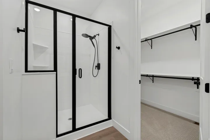 Black-framed glass shower enclosure with matte black fixtures, built-in shower shelf, and recessed lighting