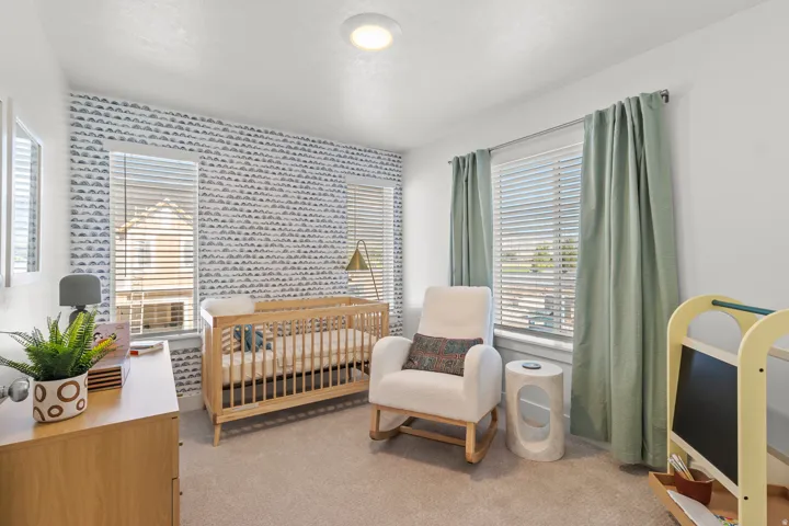 Recessed ceiling lighting illuminates a room featuring a patterned accent wall, three windows with blinds, and neutral carpeting