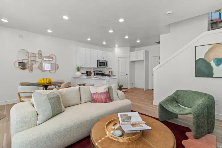 Open-concept living area with wood-finish flooring, recessed lighting, and a kitchen featuring white cabinetry and stainless steel appliances