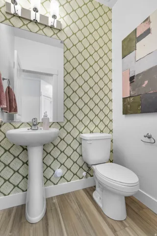 Pedestal sink with chrome faucet, toilet, and wood-finish flooring