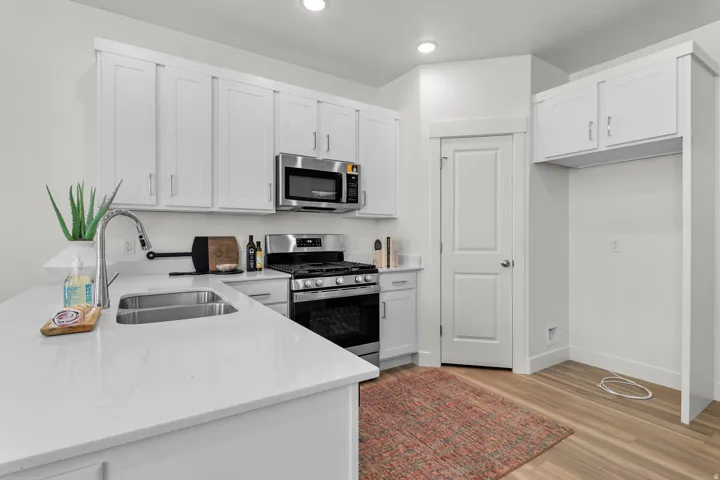 Kitchen featuring white cabinetry, stainless steel appliances, a double basin sink, light-toned countertops, and wood-finish flooring