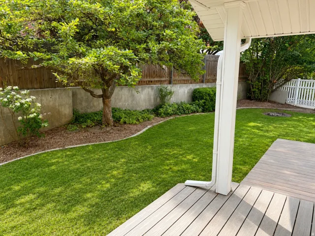 Expansive lawn with a mature tree, concrete retaining wall, white picket fence, and a composite deck