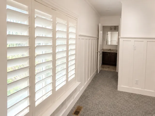 White plantation shutters, wainscoting, and gray carpeting