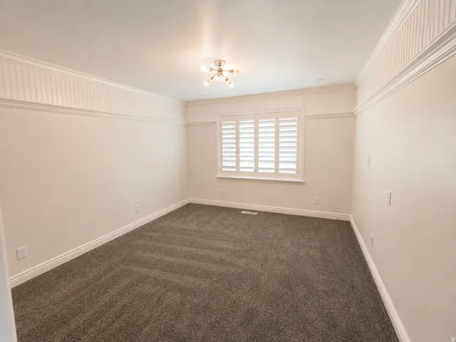 Neutral wall color, plush carpeting, window with plantation shutters, ceiling-mounted light fixture, and decorative wall trim