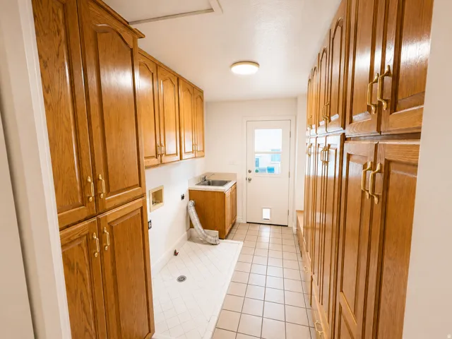 Extensive wood-finish cabinetry, utility sink, tile flooring, and exterior door with frosted glass panel